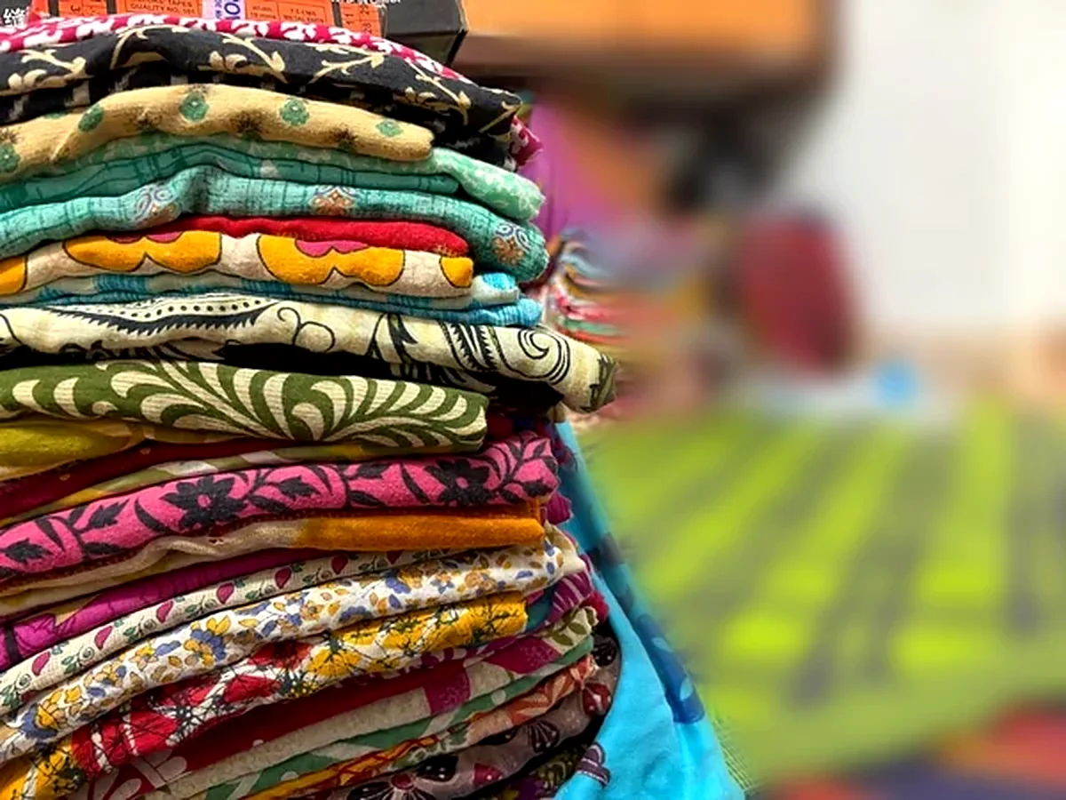 Stacks of folded, brightly patterned sari fabric waiting to be stitched.