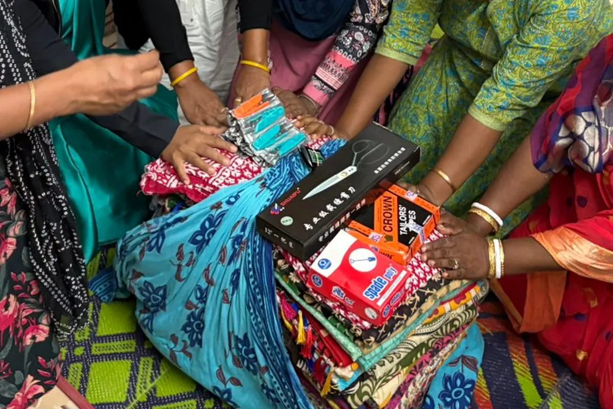 Hands gathered in prayer over stacked saris and sewing supplies.