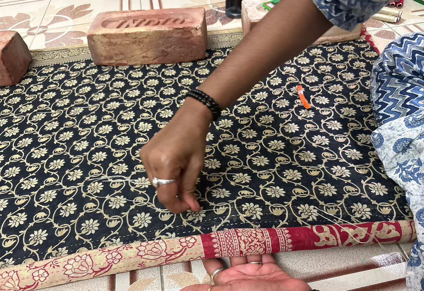 A woman's hands quilting a black and gold block-printed sari, weighted down with bricks.
