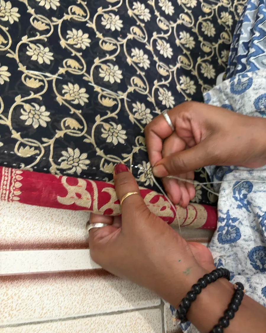 Hands threading a needle over block-printed fabric.
